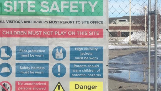 Site safety sign at construction site hanging on fence indicating dangers and being cautious. 
