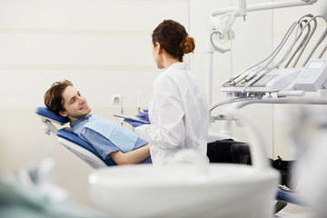 Portrait of smiling young man sitting in dentists chair during consultation, copy space