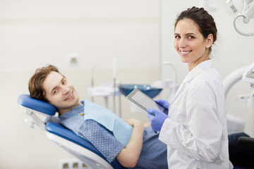 Fototapeta premium Waist up portrait of female dentist smiling happily at camera while consulting patient in background, copy space
