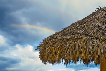 close up of tiki hut thatched roof with rainbow in sky background