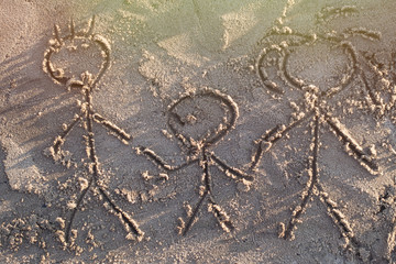 Family drawn in the sand. Three people - father, mother and child are depicted on the shore.