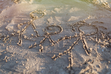 Family drawn in the sand. Three people - father, mother and child are depicted on the shore.