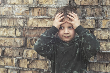 Child confused, depressed, upset. Little boy near the brick destroyed wall.