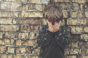 Child confused, depressed, upset. Little boy near the brick destroyed wall.