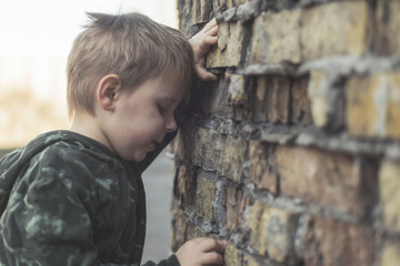 Obraz na płótnie Canvas Child confused, depressed, upset. Little boy near the brick destroyed wall.