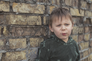Child confused, depressed, upset. Little boy near the brick destroyed wall.