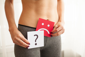 Vaginal or urinary infection and problems concept. Young woman holds paper with sad smile above crotch