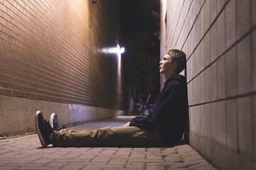 Sad teen sitting in an alleyway all alone at night.