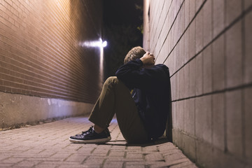 Sad teen sitting in an alleyway all alone at night.