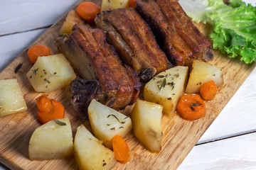 Roasted pork ribs with thyme potatoes over white wooden background, Eastern cuisine