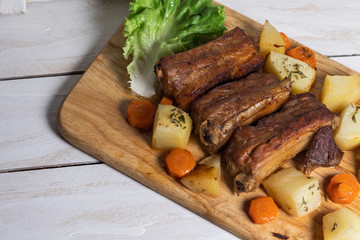 Roasted pork ribs with thyme potatoes over white wooden background, Eastern cuisine
