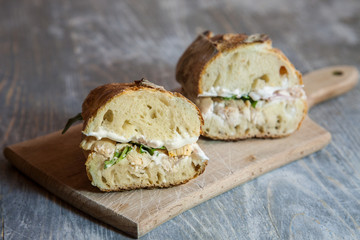 Chicken  with cream cheese in a French baguette, cut in two, with some slices of rucola salad and chicken dressing on a rustic wooden table. This sandwich, in France, is called sandwich au poulet