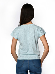 From behind. Young beautiful woman posing in gray light shirt blouse and blue jeans on a white 