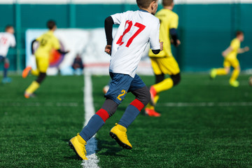 Boys in yellow white sportswear running on soccer field. Young footballers dribble and kick football ball in game. Training, active lifestyle, sport, children activity concept 