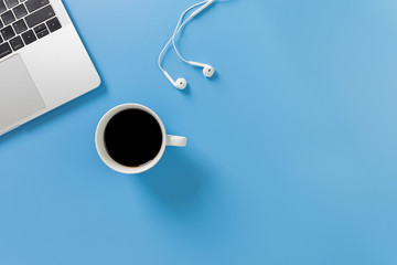 Listening to music at work. Flat lay desk top with laptop, earphone, coffee on blue background. Cool tone.