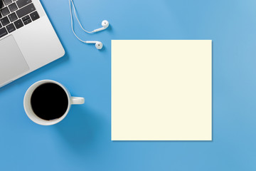 Listening to music at work. Flat lay desk top with laptop, earphone, coffee on blue background. Cool tone. paper card note.