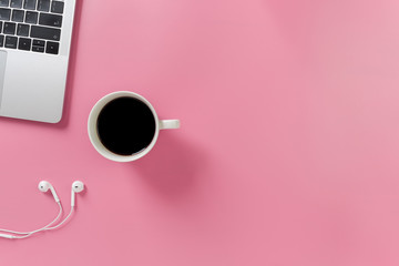 Listening to music at work. Flat lay desk top with laptop, earphone, coffee on pink background....