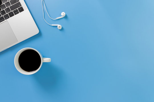 Listening To Music At Work. Flat Lay Desk Top With Laptop, Earphone, Coffee On Blue Background. Cool Tone.