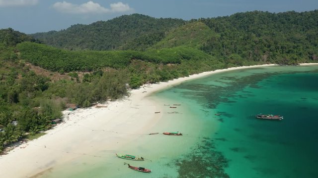Aerial drone view flying along a tropical island with sandy beach and traditional wooden boats (Swinton Island, Myanmar)