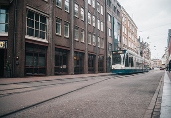 Modern public transport in Amsterdam, Netherlands. White and blue tram in old city.
