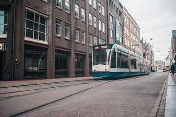 Naklejka na ściany i meble Modern public transport in Amsterdam, Netherlands. White and blue tram in old city.