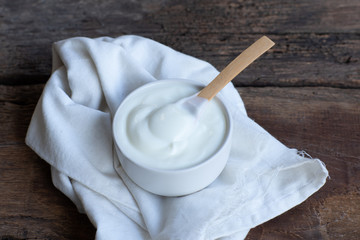 Natural homemade plain organic yogurt in bowl and wood spoon on wood texture background