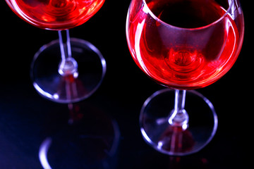 Two Glasses of red wine in night club on black background with reflection.