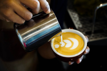 Close up barista hands pouring froth milk in espresso coffee cup for making latte art