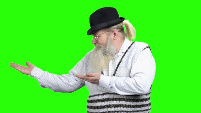 Senior businessman showing copy space for clients. Positive bearded man in hat showing copy space for advertising on green screen.