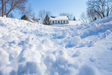 Snow drifts and chunks of snow piling up in winter with a house in the background