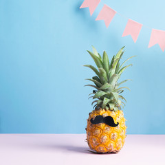 Funny dressed up pineapple with a black mustache on a pastel blue background with festive pink flags. Minimalism. Art.