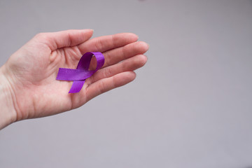 Girl’s hand holding light violet ribbon, symbol of  pancreatic cancer, cancer awareness month.