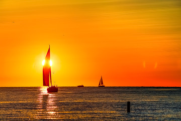 Sailing yacht at sunset, sun setting behind the sail