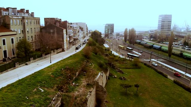 Aerial drone shot left-right panoramic movement revealing the Roman edifice with mosaic, the traffic of Constanta, Romania, and the shipyard in a foggy spring day