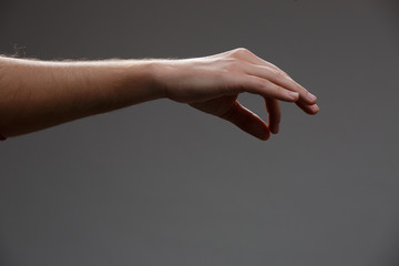 Photo of outstretched hand holding something with two fingers on empty gray background.