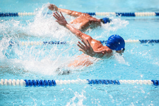 Men swimming butterfly stroke in a race, focus on water droplets,  swimmer is out of focus