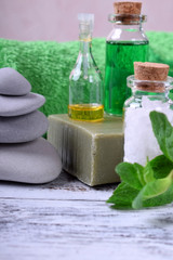 Spa set: massage stones, aromatic oil, sea salt, green gel, organic soap and green towel on white wooden table