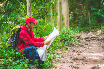 Asian traveller man searching right direction on map in the forest with copy space.