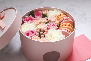 Gift round box with flowers, roses and macaroons almond cake with pink envelope on the table