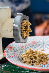 Meat grinder cutting, grinding nuts, walnuts onto plate.