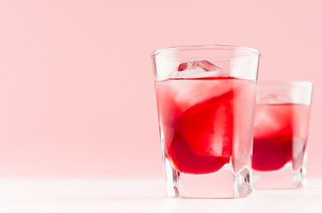 Fresh cold red summer fruit cocktails with ice cubes in elegant modern kitchen interior in light soft pastel pink color on white wood board.