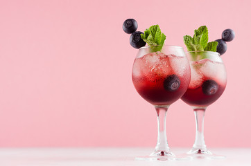 Luxury fresh cold red summer fruit cocktails with ice cubes, blueberry, green mint in elegant modern kitchen interior in light soft pastel pink color.