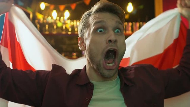 Emotional male fan waving flag of England in pub rejoicing national team victory