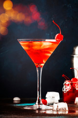 Classic alcoholic cocktail Manhattan with bourbon, red vemuth, bitter, ice and cocktail cherry in glass, gray bar counter background, place for text, selective focus