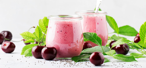 Pink cherry smoothies with fresh red berry and chia seeds, green leaves, white stone kitchen...