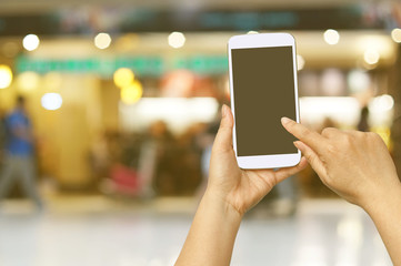 Hand hold and touch screen with Blur shopping mall background.