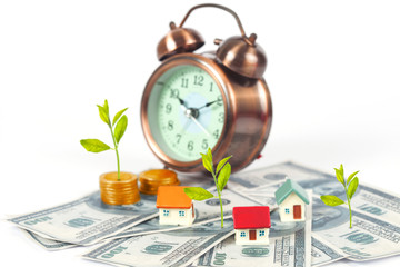 mini house on coin stack with alarm clock and grow plant
