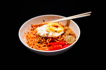 A bowl of spicy noodles with eggs and chili ready to eat with chopsticks