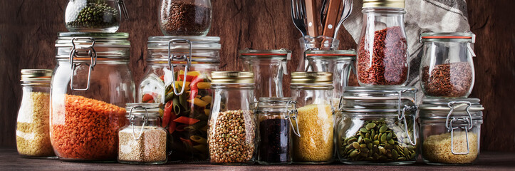 Food set. Raw cereals, pasta, groats, organic legumes and useful seeds in glass jars. Vegan source of protein and energy resources. Rustic wooden kitchen table background. Banner