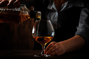 The bartender pours the cognac or brandy in big wine glass on the old bar counter. Vintage wooden...